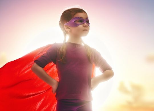 Little child girl plays superhero. Child on the background of sunset sky. Girl power concept