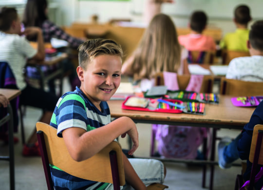 Happy little boy turning towards the camera during the lecture in the classroom.